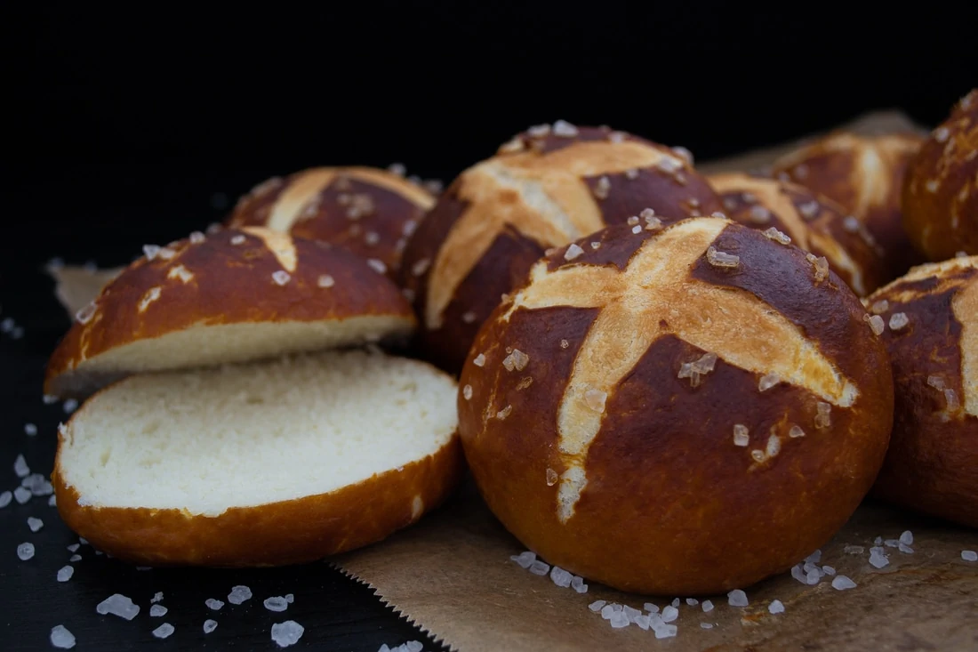 Frisch gebackene, braune Laugenbrötchen, bestreut mit groben Meersalz, liegen auf einem Backpapier.