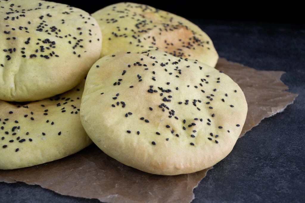 Luftige Pita-Taschen bestreut mit schwarzem Sesam liegen auf einem Backpapier.