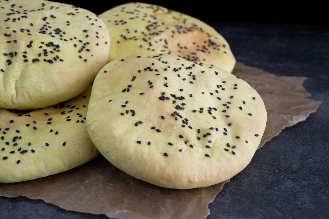Luftige Pita-Taschen bestreut mit schwarzem Sesam liegen auf einem Backpapier.