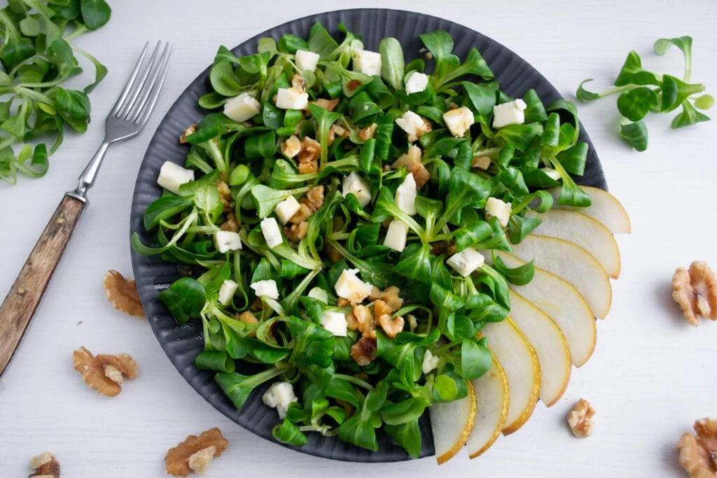 Feldsalat mit Gorgonzola, Birne und Walnüssen angerichtet auf einem schwarzen Teller