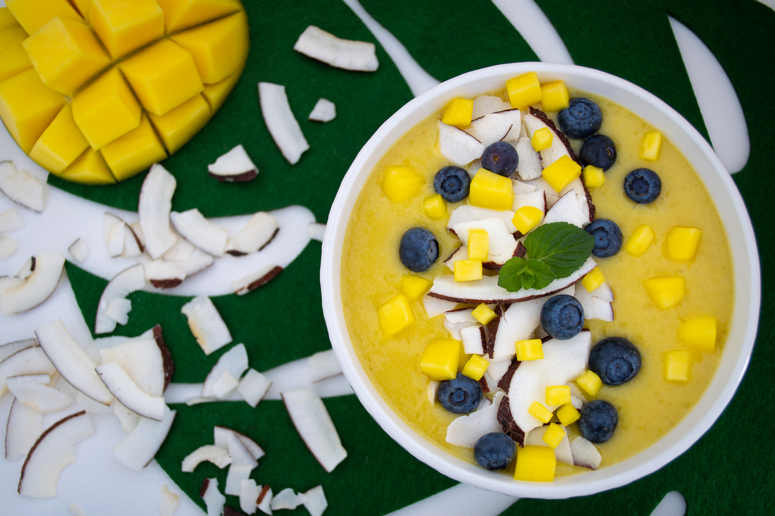 Mango-Kokos Bowl mit Kokoschips, Heidelbeeren und Mangowürfel in weißer Schale