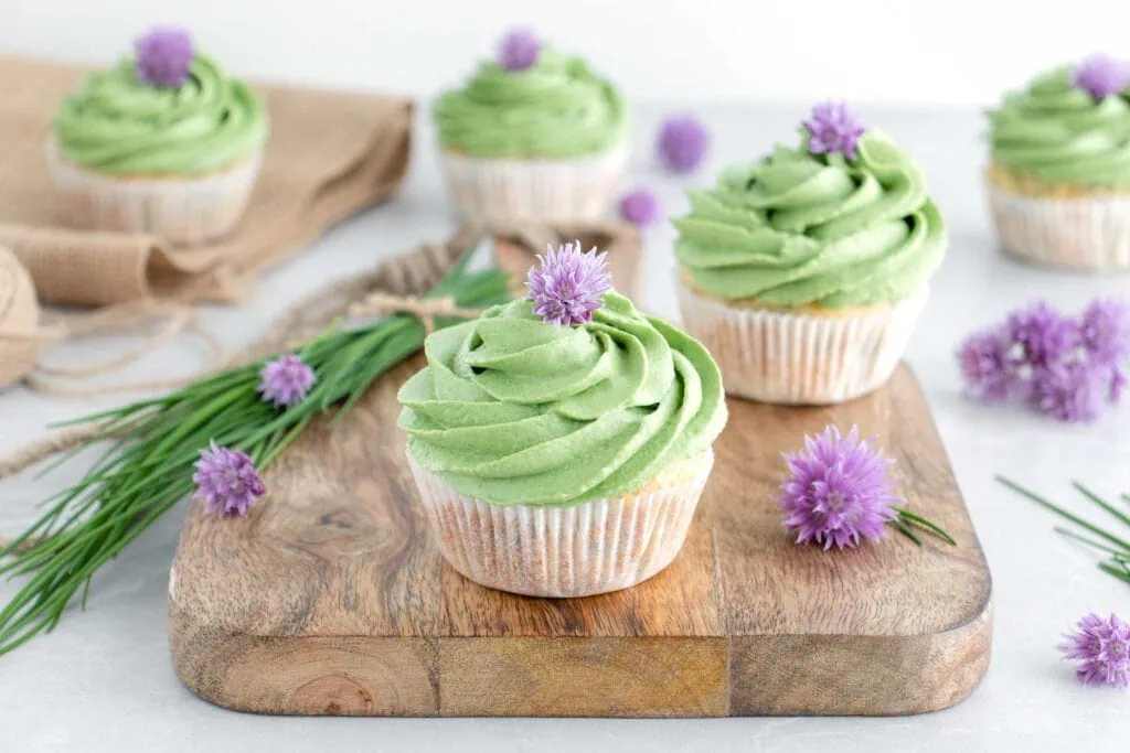 Herzhafte Muffins mit Frischkäse-Frosting, garniert mit lila Schnittlauchblüten, liegen auf einem Holzbrett.