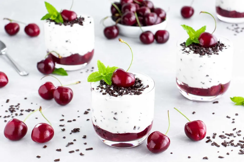 Stracciatella Creme mit Kirschen im Glas garniert mit einem Blatt frischer Minze