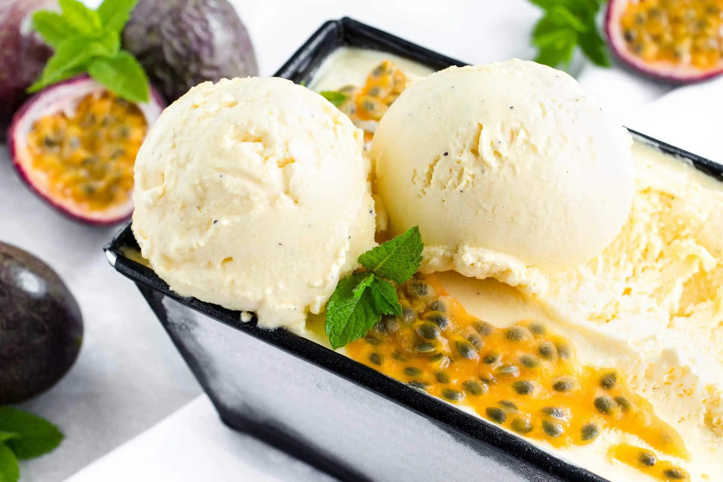 Maracuja-Eis Kugeln in einem Eisbehälter garniert mit dem Fruchtfleisch einer Maracuja und frischer Minze.
