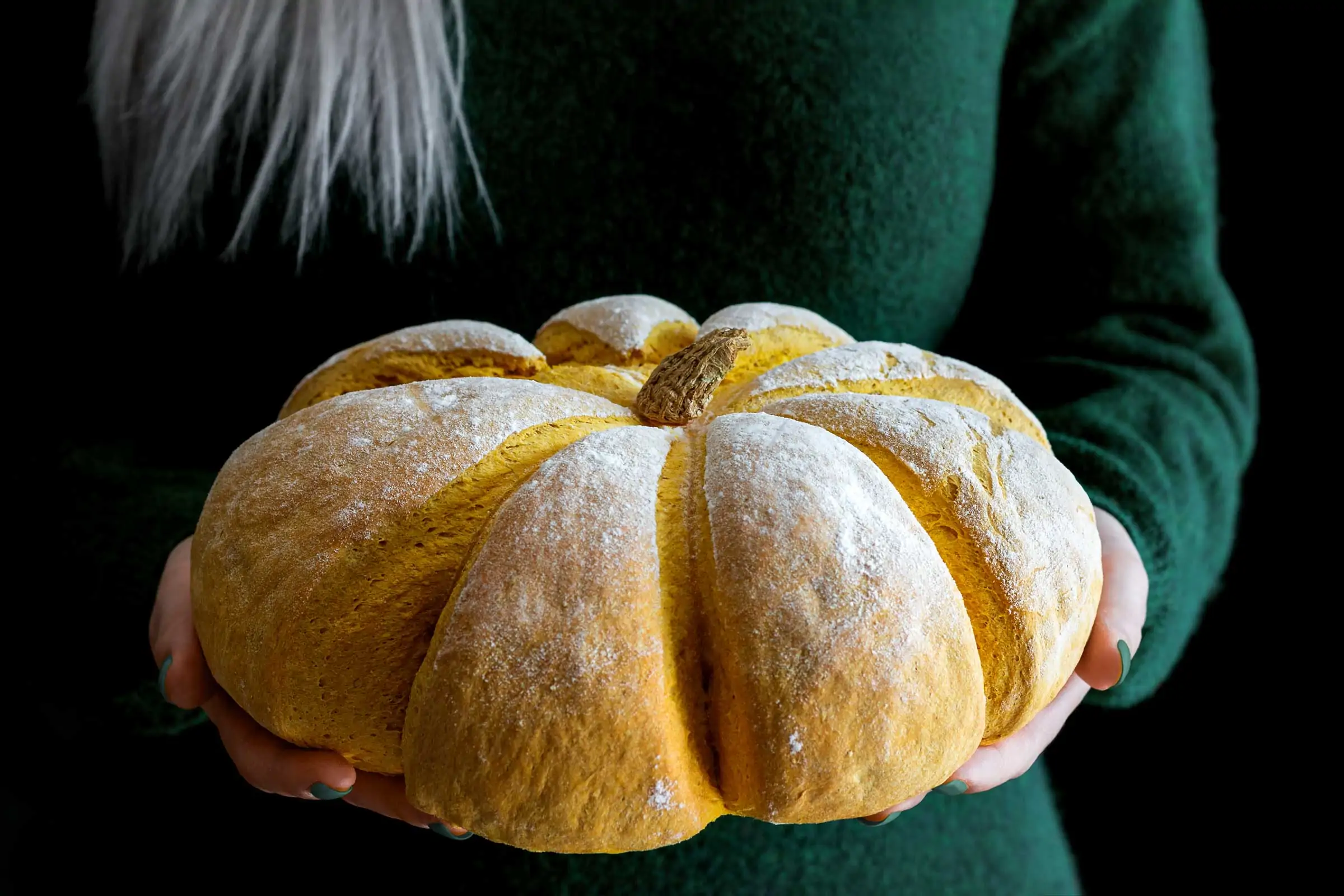 Kürbisbrot in der Farbe und Form eines Kürbisses wird von einer Frau in den Händen gehalten.