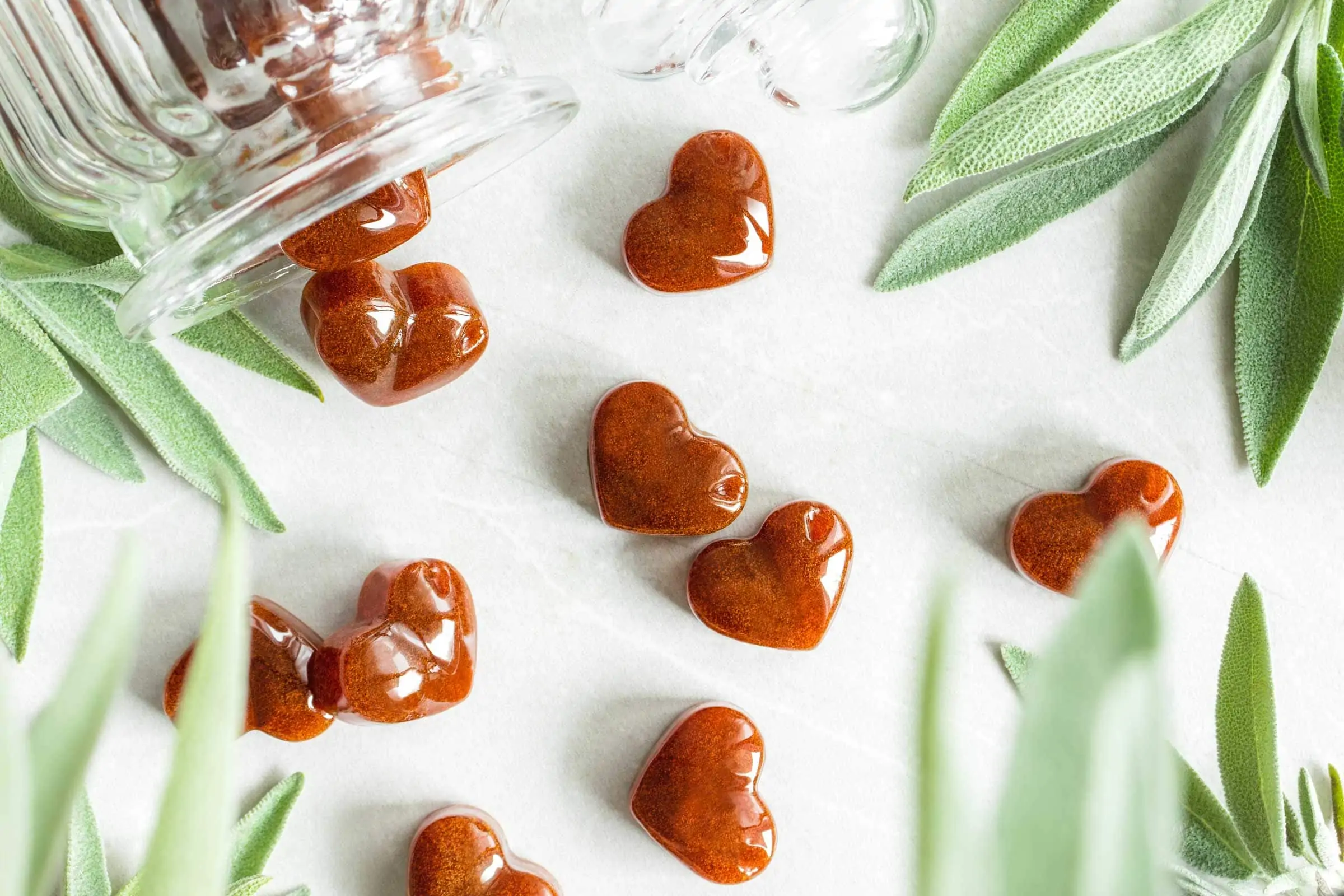 Salbeibonbons liegen neben mehreren Blättern frischem Salbei und einem Bonbonglas.