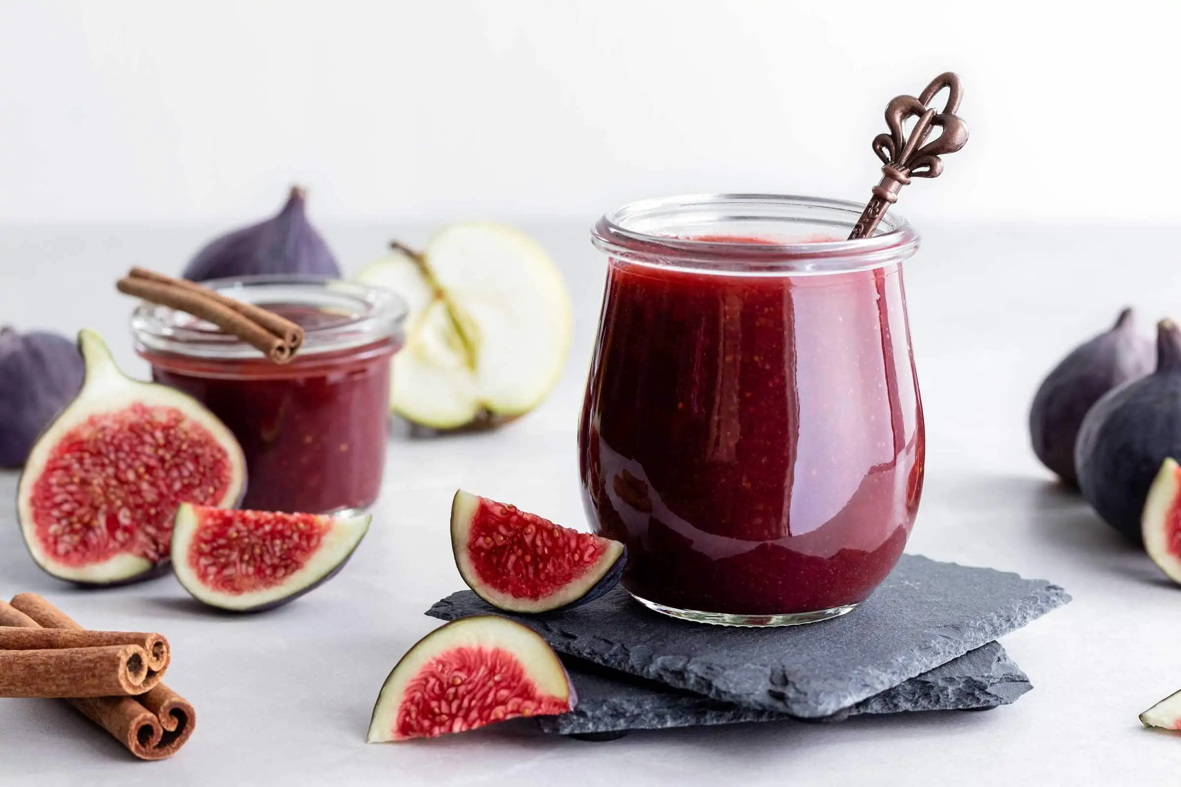 Feigenmarmelade mit Apfel und Zimt in einem Glas. Neben der Marmelade liegen frische Feigen und Zimtstangen.