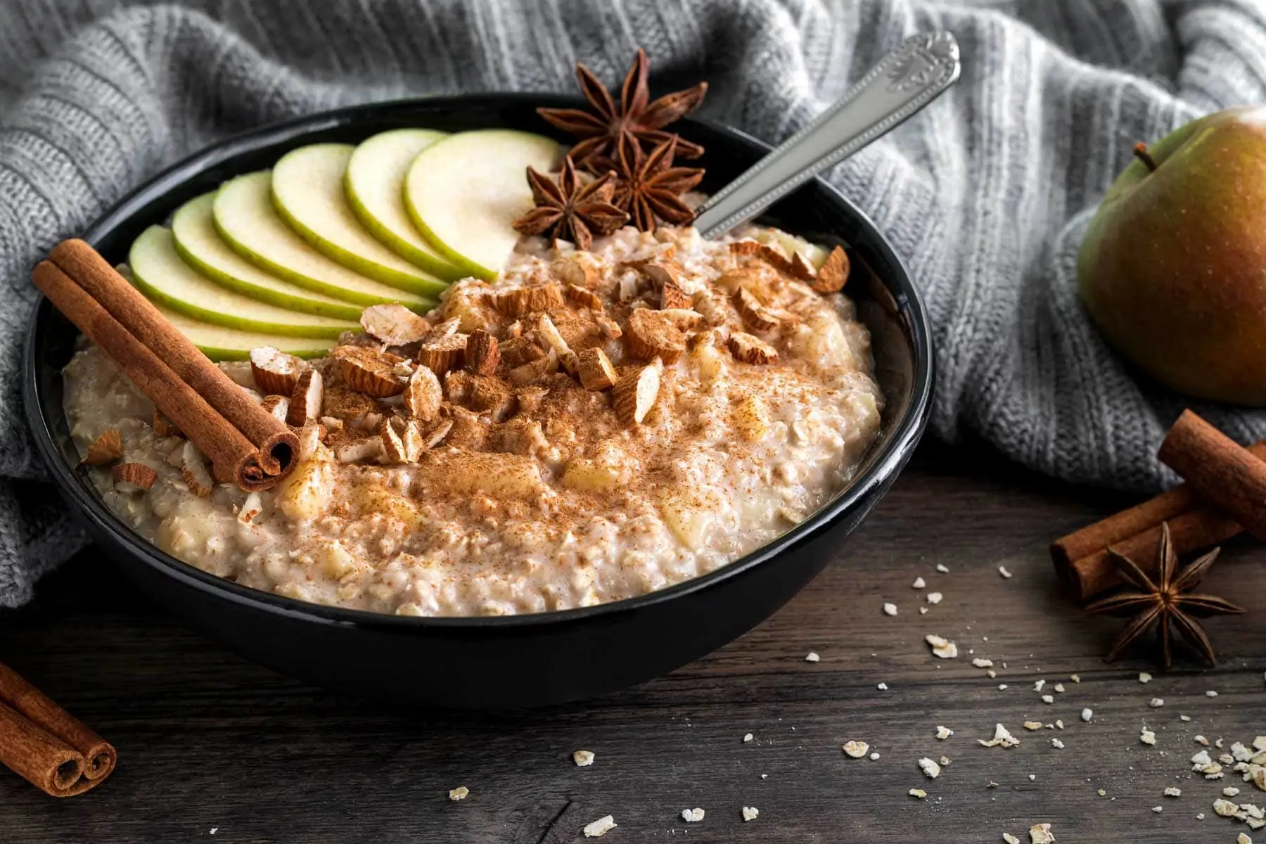 Warmes Porridge mit Apfel und Zimt in einer Schüssel garniert mit Apfelstücken, Sternanis und einer Zimtstange.