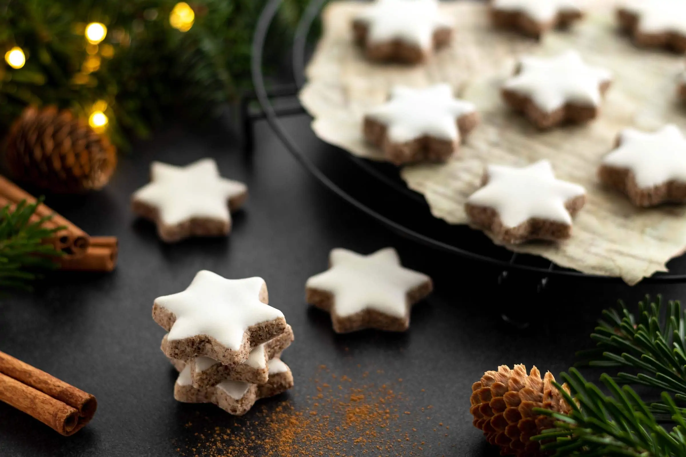 Klassische Zimtsterne gestapelt zu einem kleinen Türmchen. Hinter den Zimtsternen steht ein Abkühlgitter mit weiteren Plätzchen.