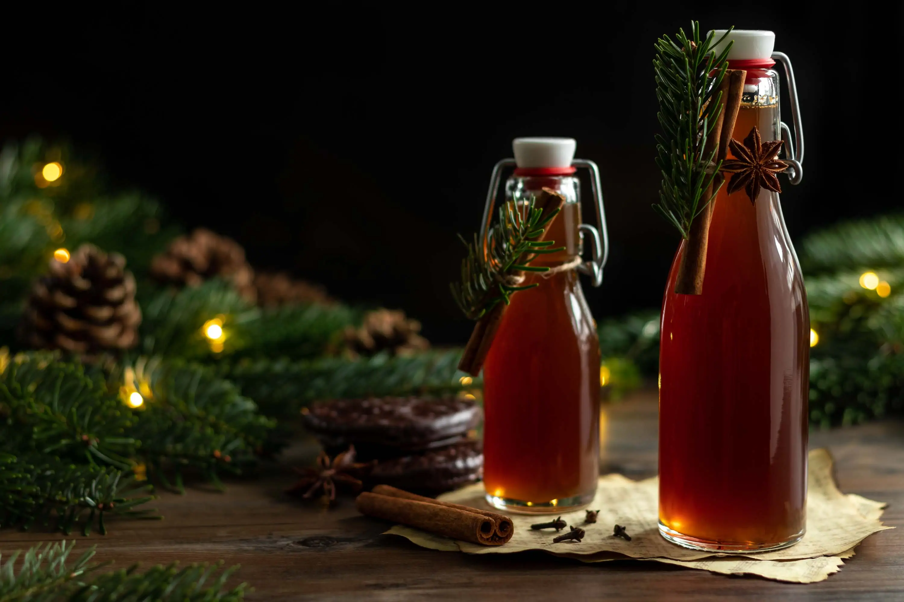 Lebkuchensirup abgefüllt in zwei Bügelverschlussflaschen. Neben dem Sirup liegen Tannenzweige, Gewürze und Lebkuchen.