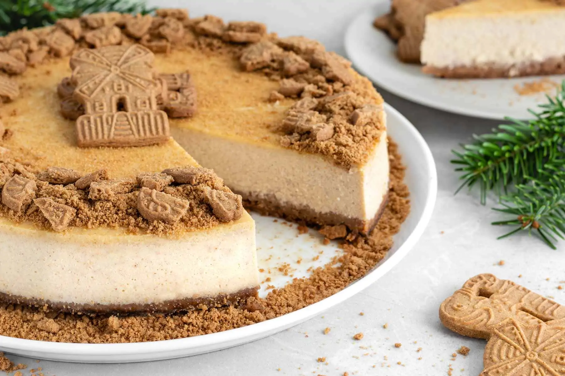 Spekulatius Cheesecake in New York Style, garniert mit Spekulatiuskeksen auf einer weißen Kuchenplatte.