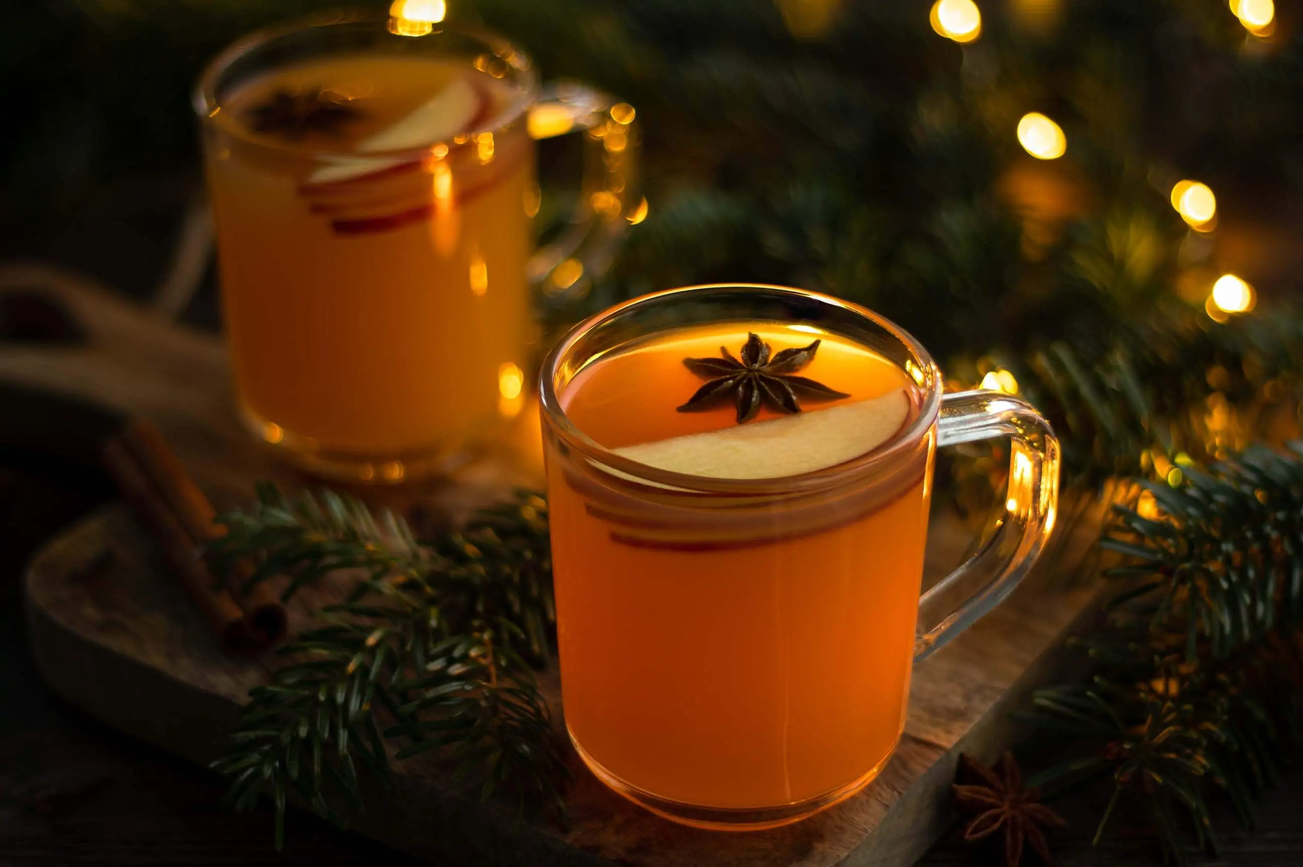 Heißer Apfelpunsch mit Amaretto in einer Tasse. Hinter dem Punsch liegen Tannenzweige und eine Lichterkette.