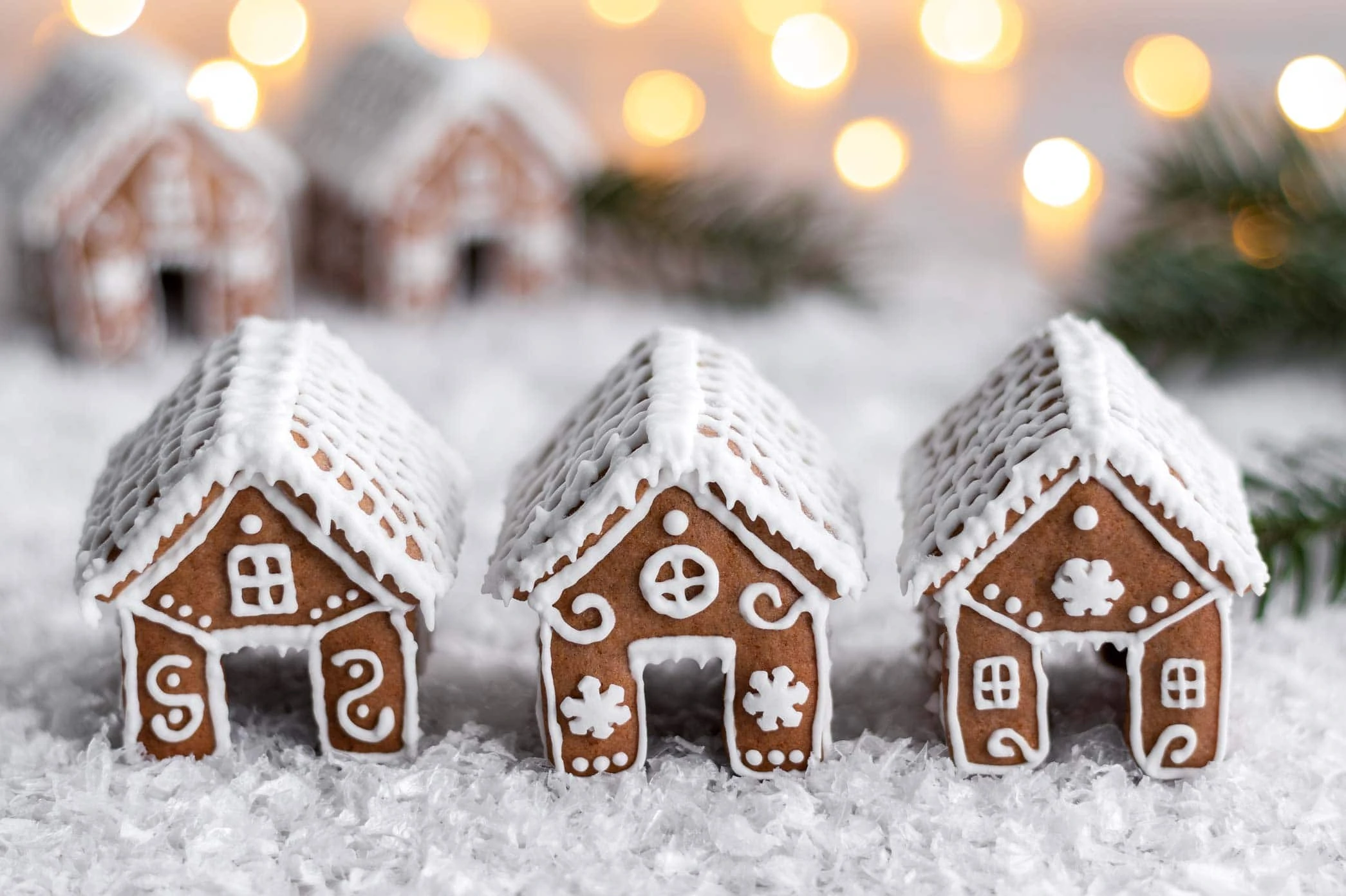 Mini-Lebkuchenhäuser vierziert mit Royal Icing auf einer Schicht aus Kunstschnee.