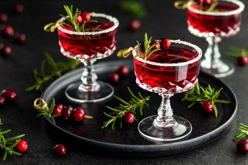 Wodka Cranberry Cocktails mit Rosmarin und frischen Cranberrys als Aperitif in einer Champagnerschale mit Zuckerrand.