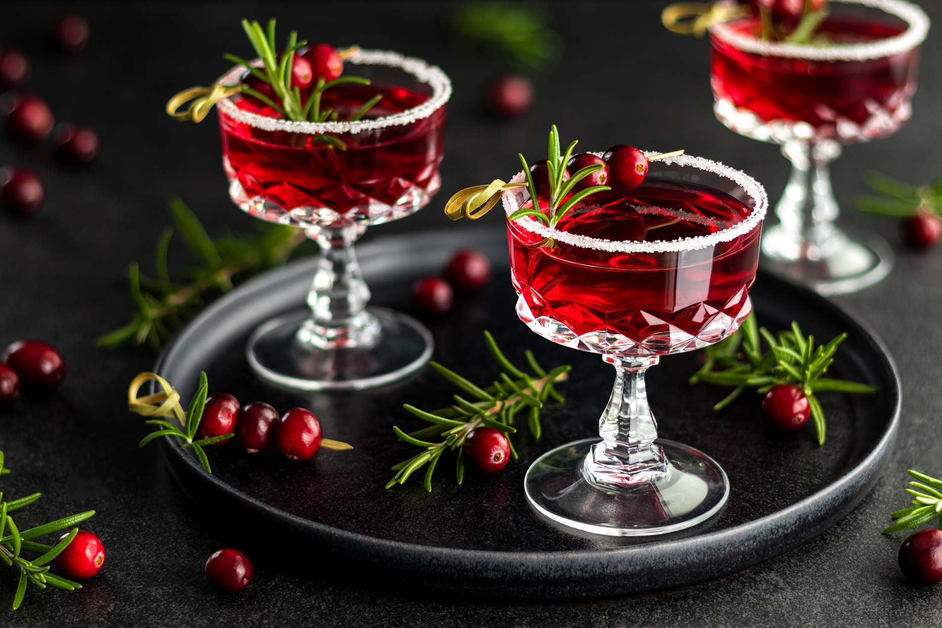 Wodka Cranberry Cocktails mit Rosmarin und frischen Cranberrys als Aperitif in einer Champagnerschale mit Zuckerrand.