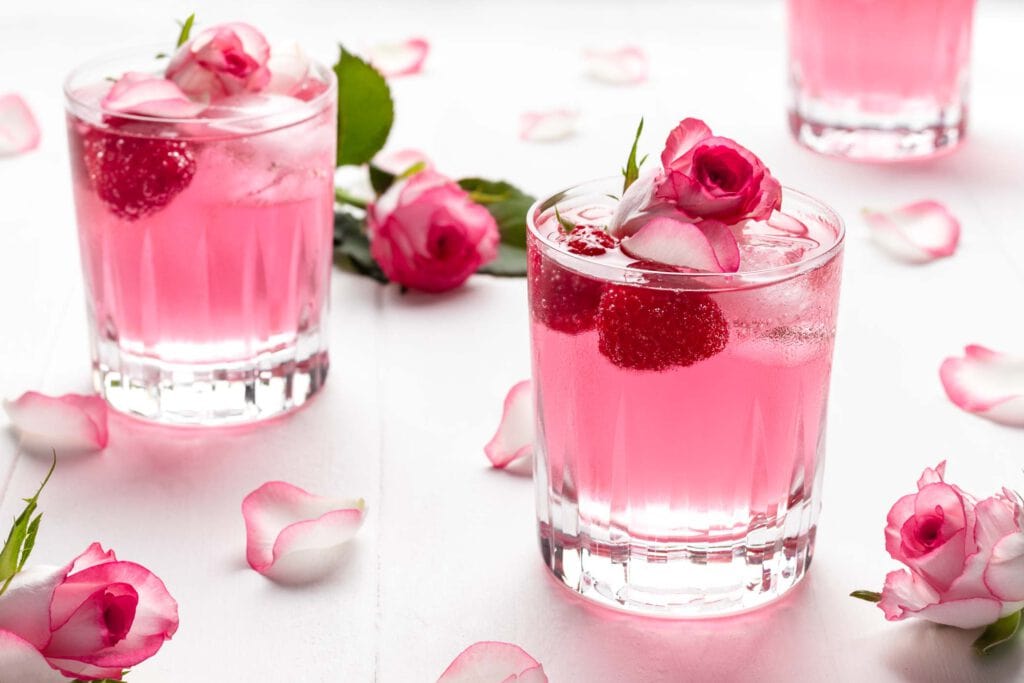Pinker Gin Wild Berry mit Rosenwasser und Himbeeren in einem kleinen Glas garniert mit Rosenblütenblättern.