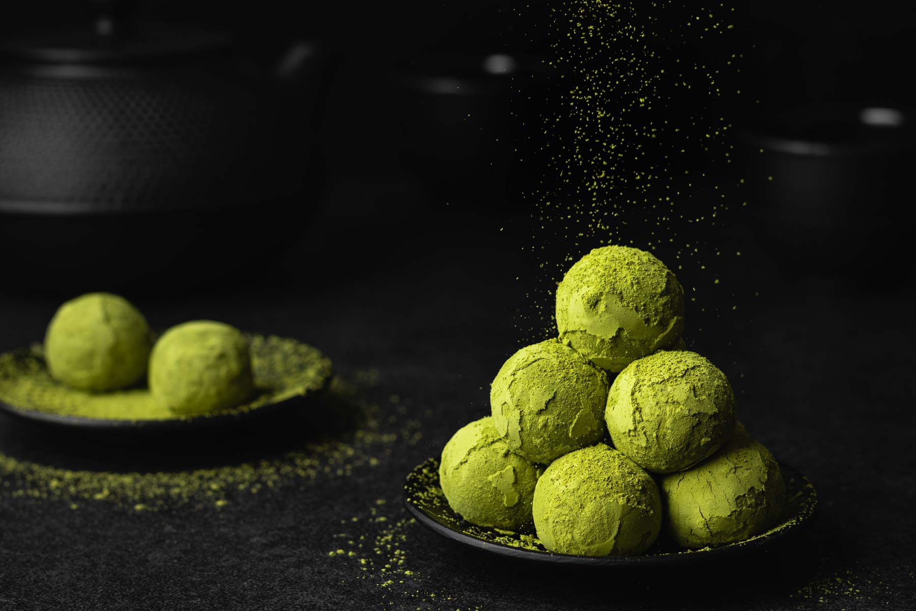 Vegane Matcha Energy Balls mit Datteln und Kokos auf einem schwarzen Teller gestapelt werden mit grünem Matcha Pulver bestreut.