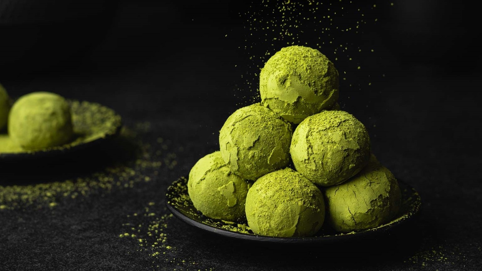 Vegane Matcha Energy Balls mit Datteln und Kokos werden mit grünem Matcha Pulver bestreut.