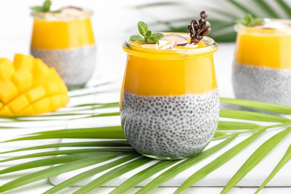 Veganer Chia Pudding mit Kokosmilch und Mango in einem Glas garniert mit Kokoschips.