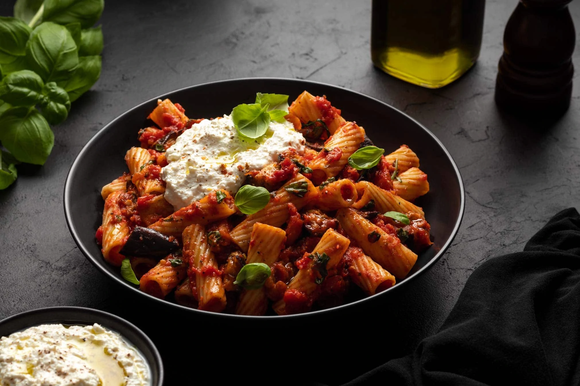 Sizilianische Pasta alla Norma mit Ricotta und Auberginen in einem tiefen Teller garniert mit Basilikum.