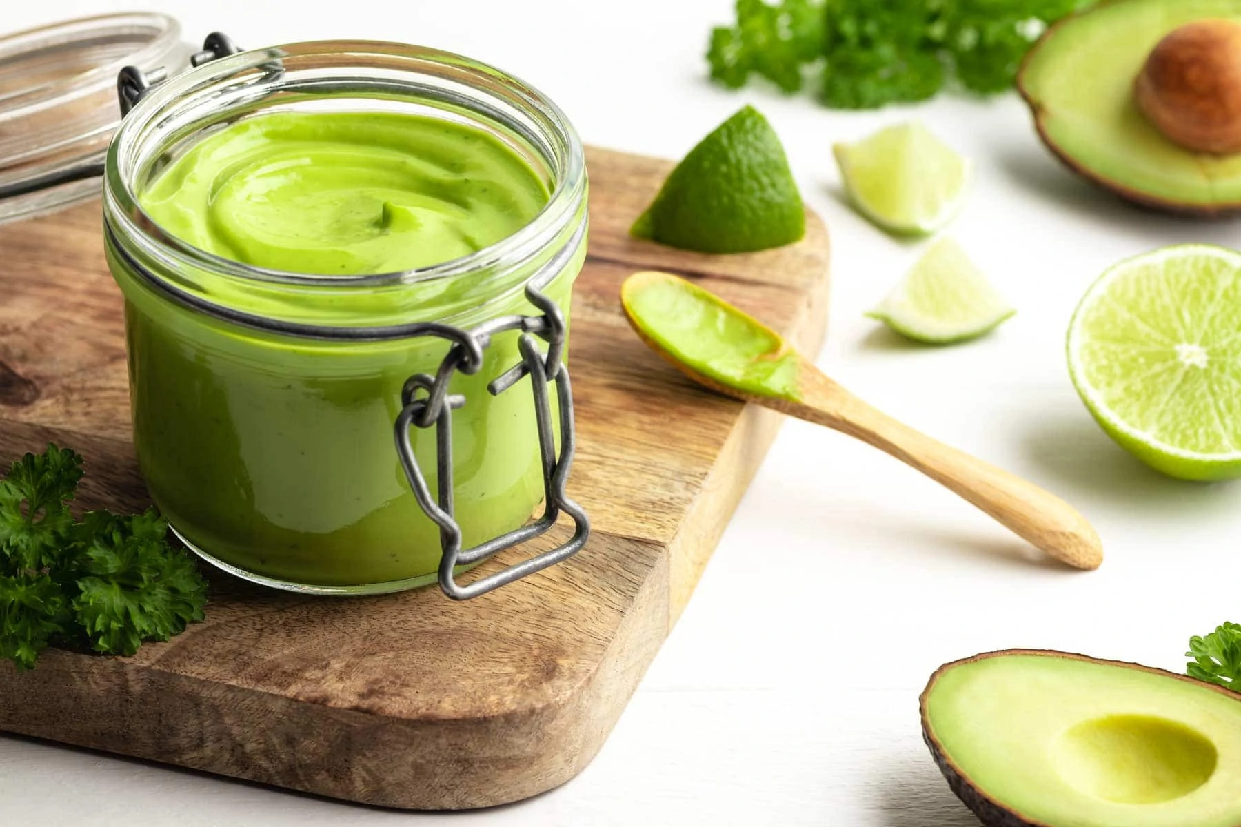 Avocado-Limetten-Mayonnaise ohne Ei in einem Glas. Daneben liegen geschnittene Avocados und Limetten.