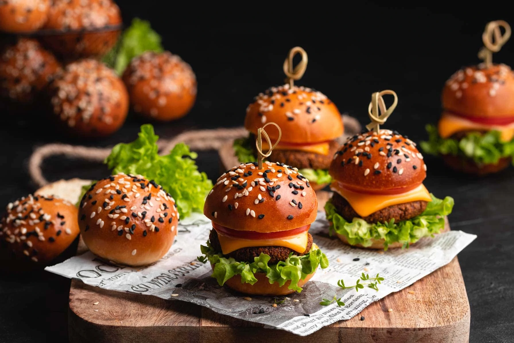 Mini Brioche Burger Buns mit Sesam und belegte kleine Fingerfood-Burger auf einem Holzbrett.