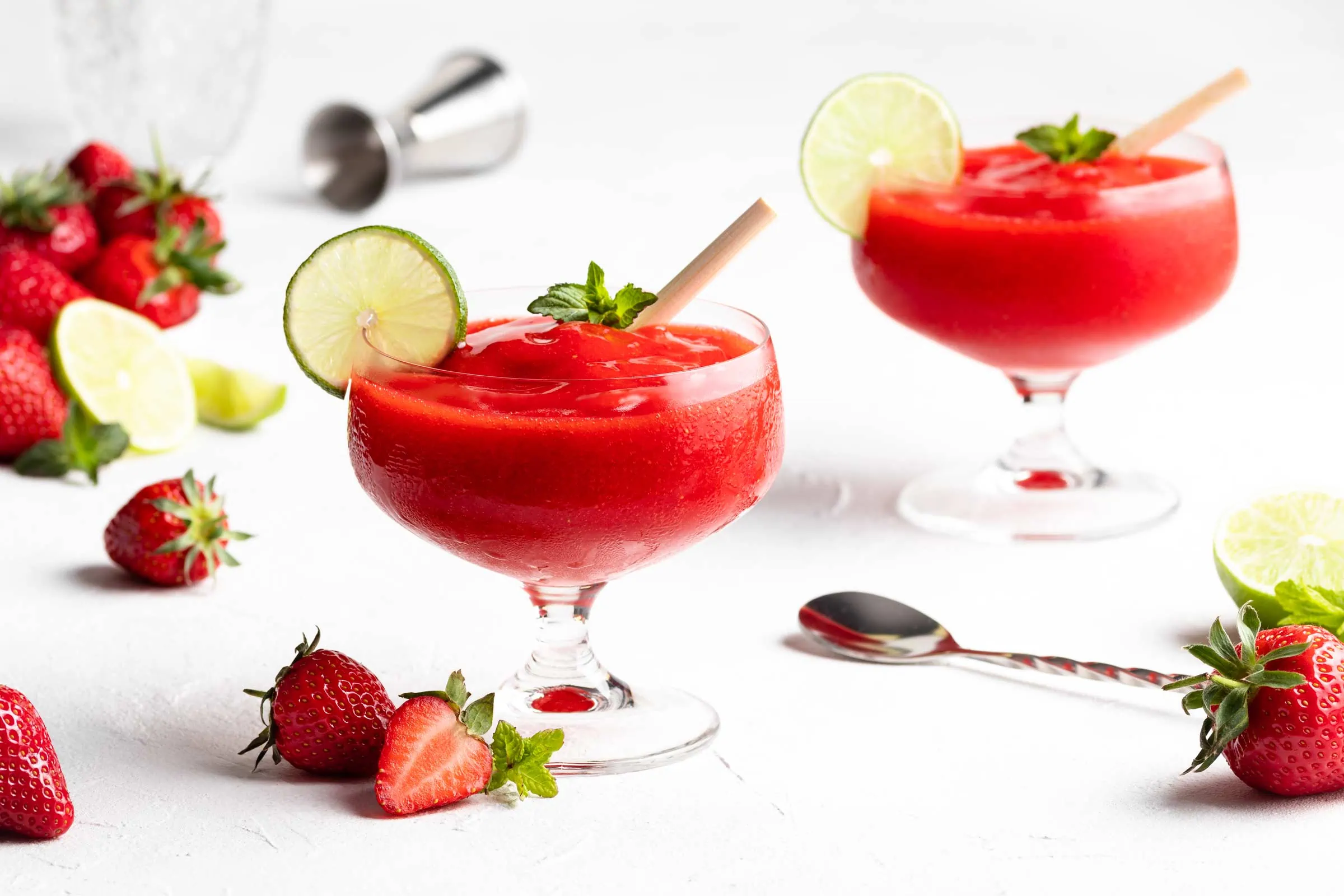 Frozen Erdbeer Daiquiri in zwei Gläsern garniert mit einer Limettenscheibe und frischen Erdbeeren.