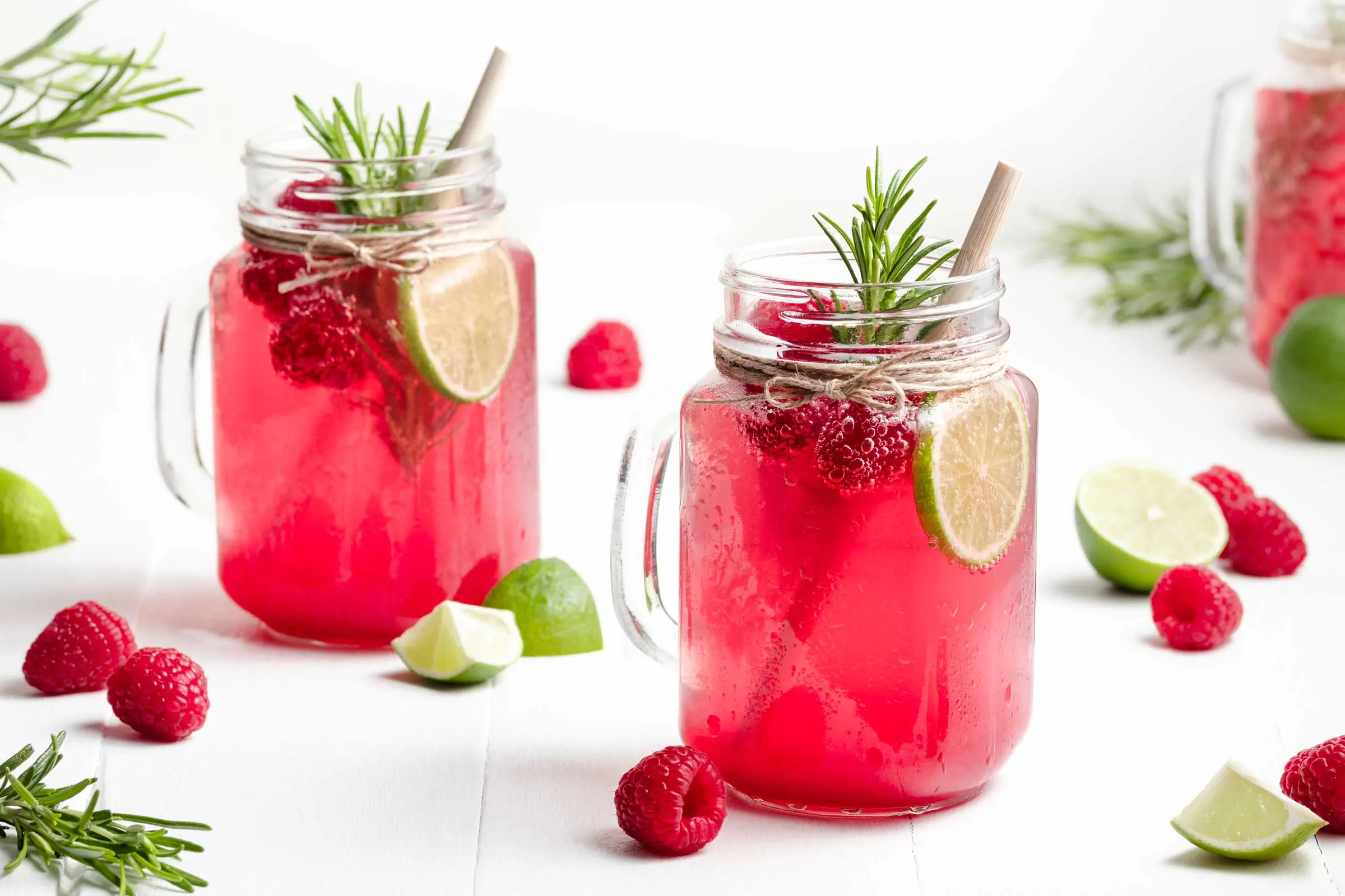 Himbeer-Limonade mit Rosmarin und Limette angerichtet in drei Gläsern mit Henkel.