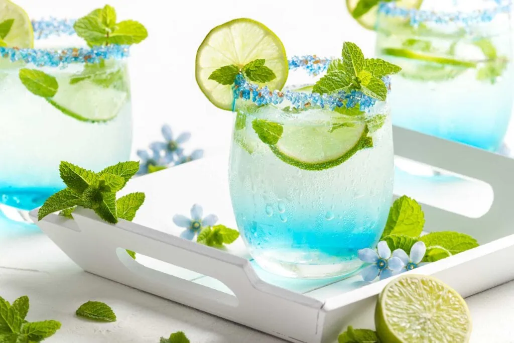 Blauer Hugo mit Blue Curaçao in einem Glas mit Zuckerrand garniert mit Limette und Minze.