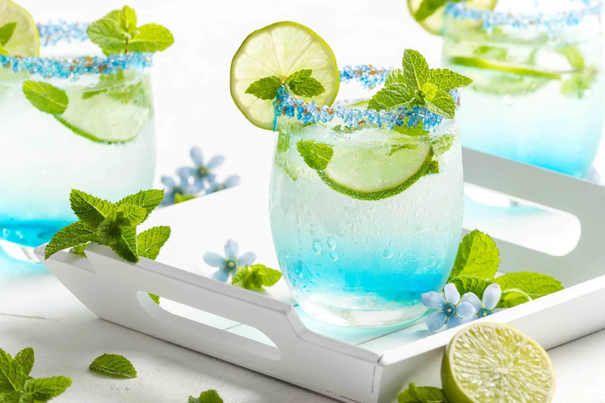 Blauer Hugo mit Blue Curaçao in einem Glas mit Zuckerrand garniert mit Limette und Minze.