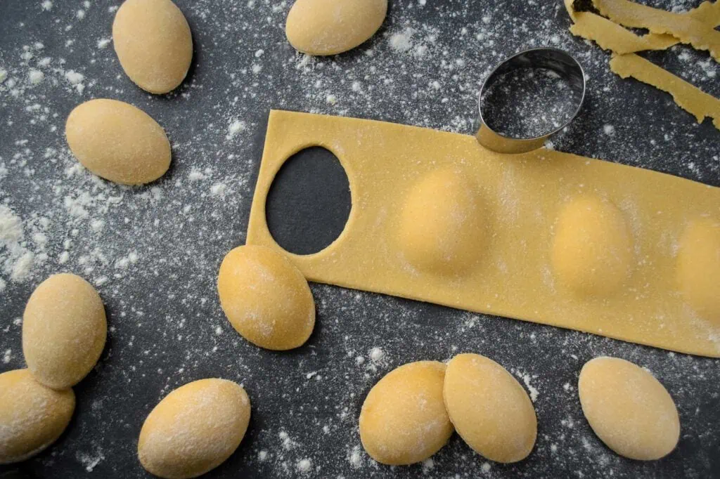 Selbstgemachten Ravioli mit Ricotta-Karotten-Füllung in Form von Ostereiern werden aus dem Nudelteig ausgestochen.