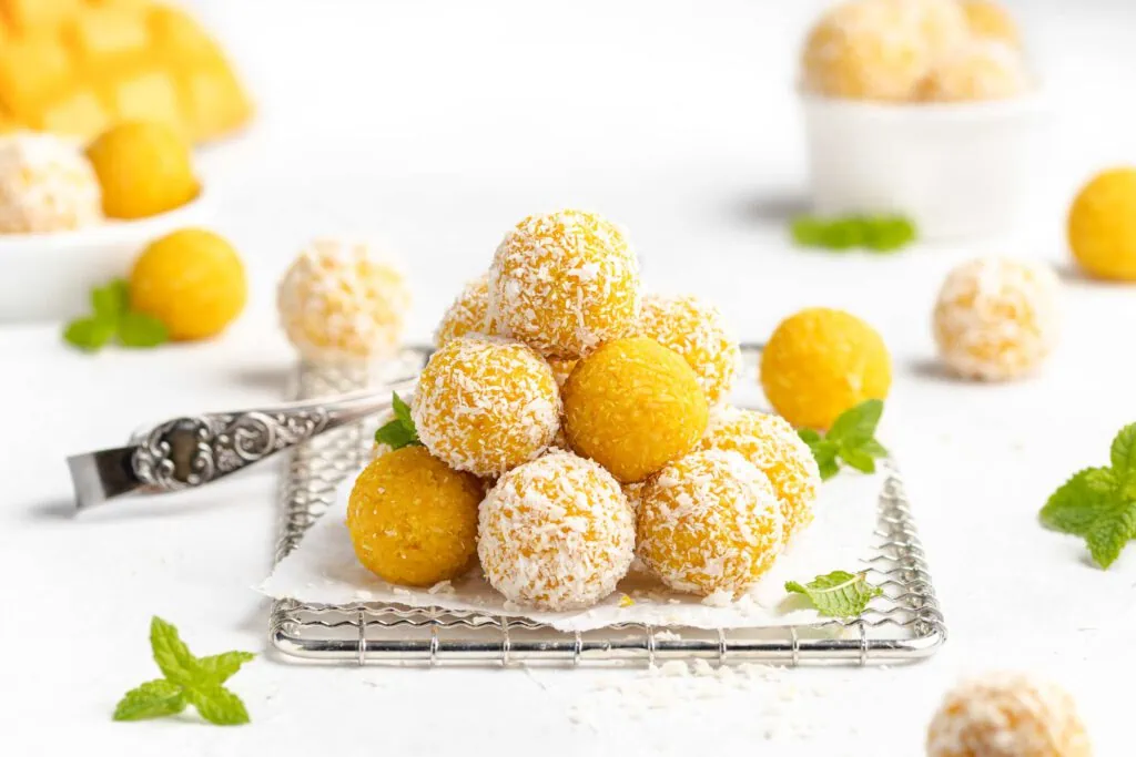Mango Ladoo gestapelt auf einem Gitter. Neben der indischen Süßigkeit liegen eine Mango und frische Minze.