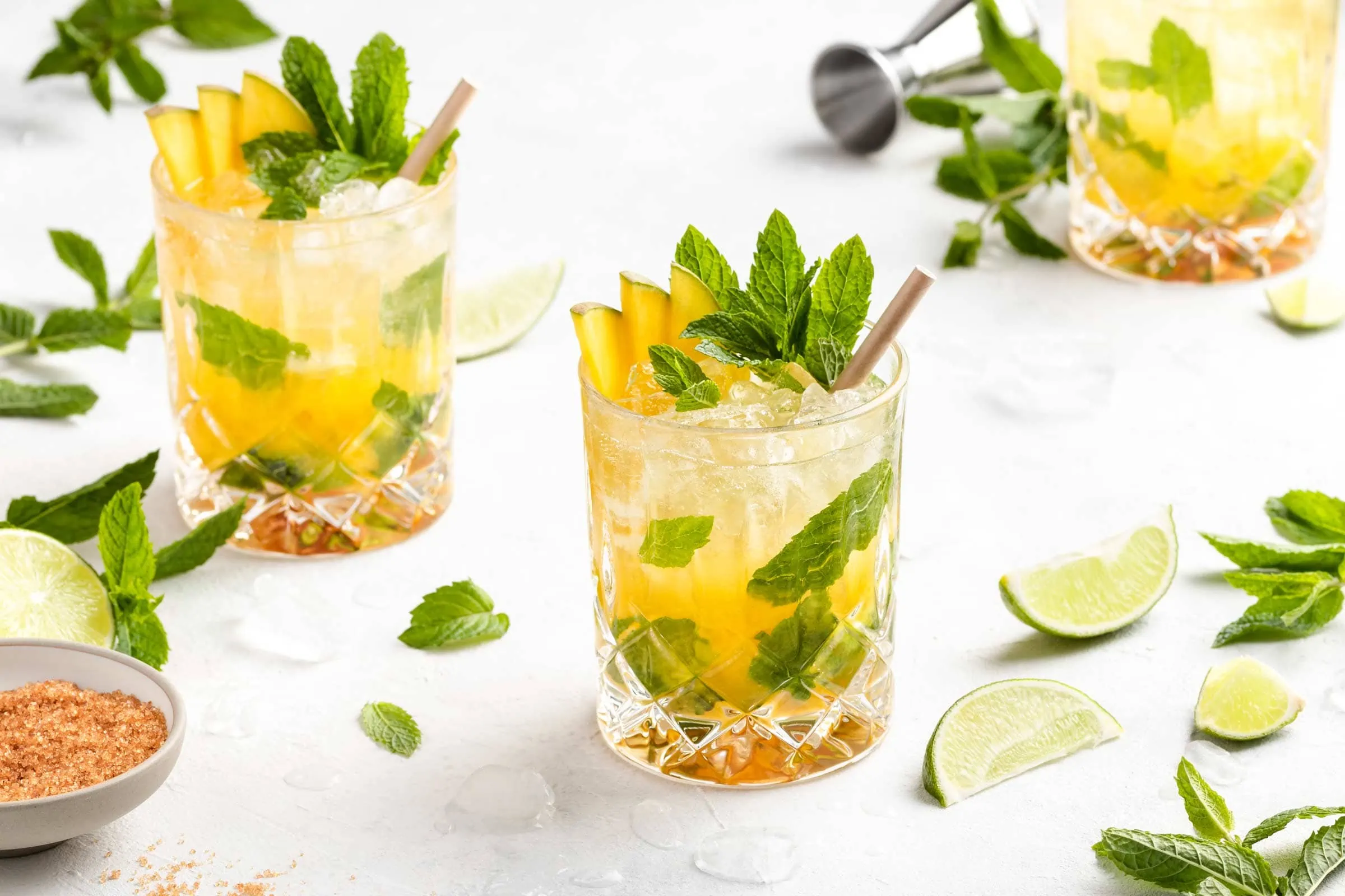 Mango Mojito mit Mangopüree und Mangosaft in Tumblern auf einem weißen Untergrund, garniert mit frischer Minze und Limette.