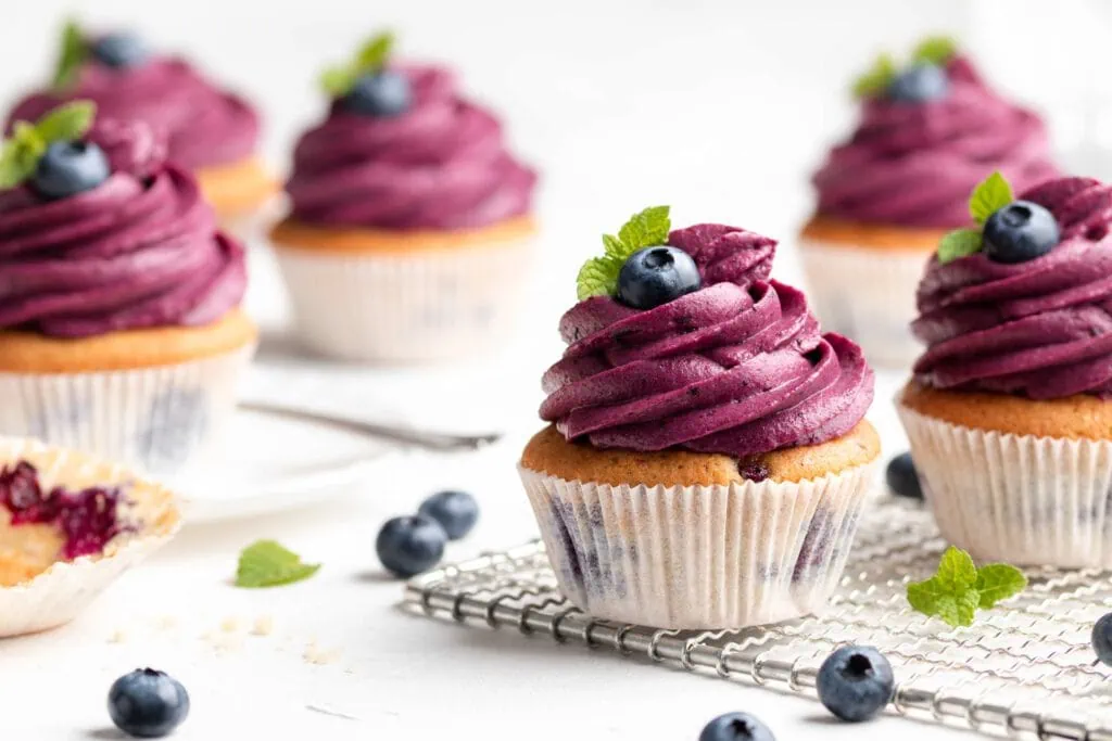Saftige Blaubeer-Cupcakes mit Frischkäse-Frosting und Blaubeeren getoppt auf einem hellen Untergrund.