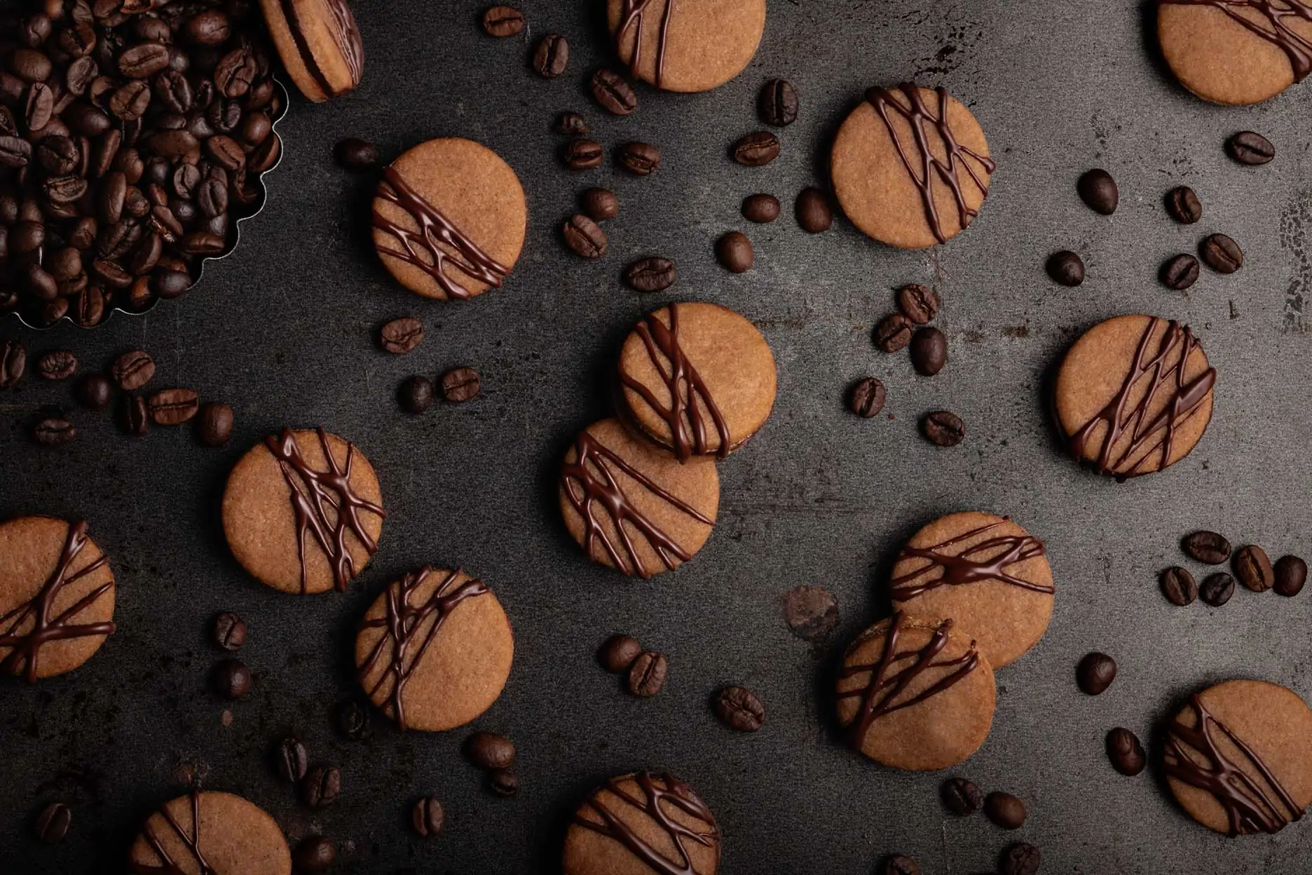 Gefüllte Kaffee Plätzchen mit Kakao liegen neben Kaffeebohnen auf einem dunklen Untergrund.