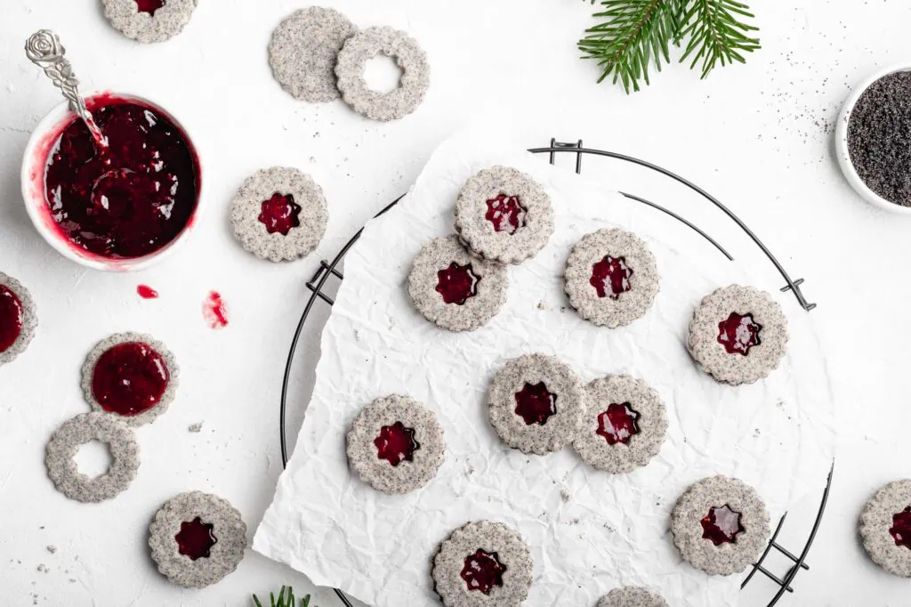 Saftige Mohnplätzchen mit Marmelade auf einem Abkühlgitter. Neben dem Gitter steht eine Schüssel mit Marmelade.