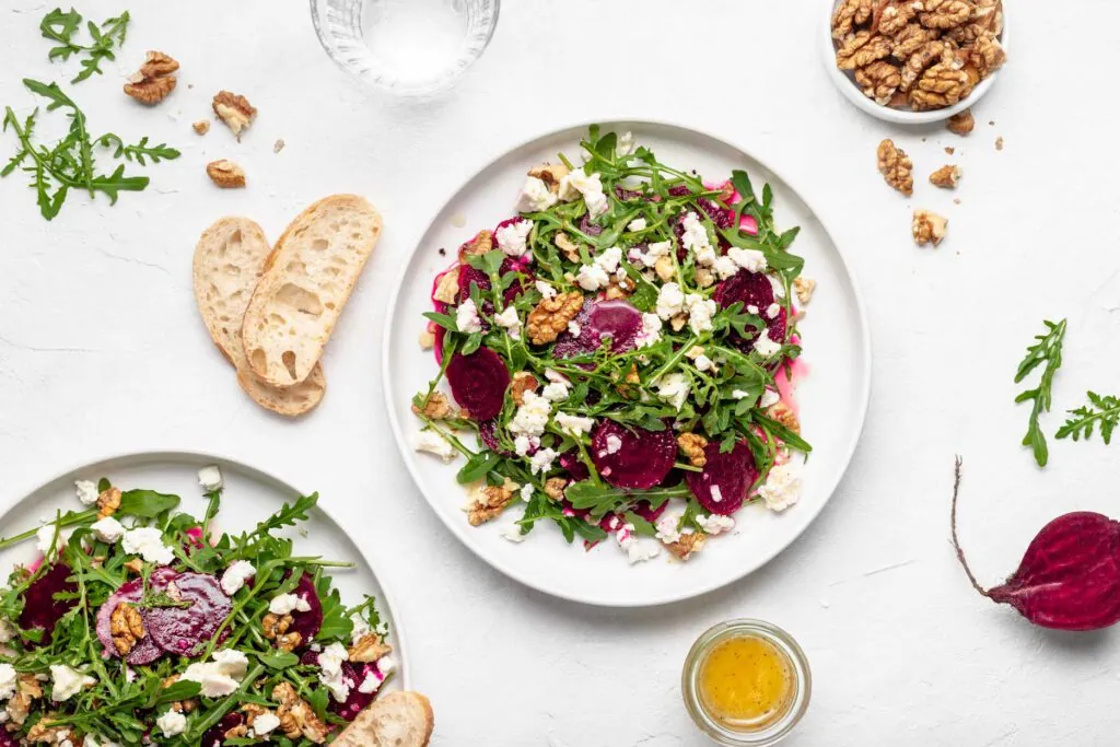 Rote Bete Salat mit Rucola, Schafskäse und Walnüssen beträufelt mit einem Dressing auf zwei Tellern.