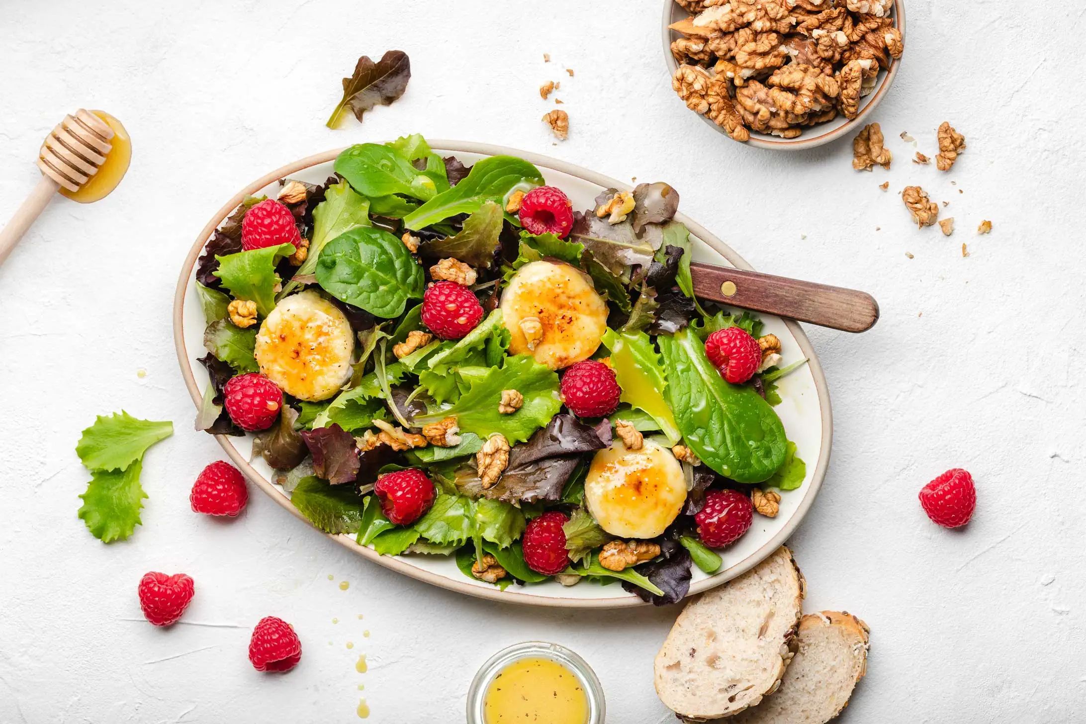 Salat mit gebackenem Ziegenkäse mit Honig und Walnüssen und frischen Himbeeren auf einem ovalen Teller.