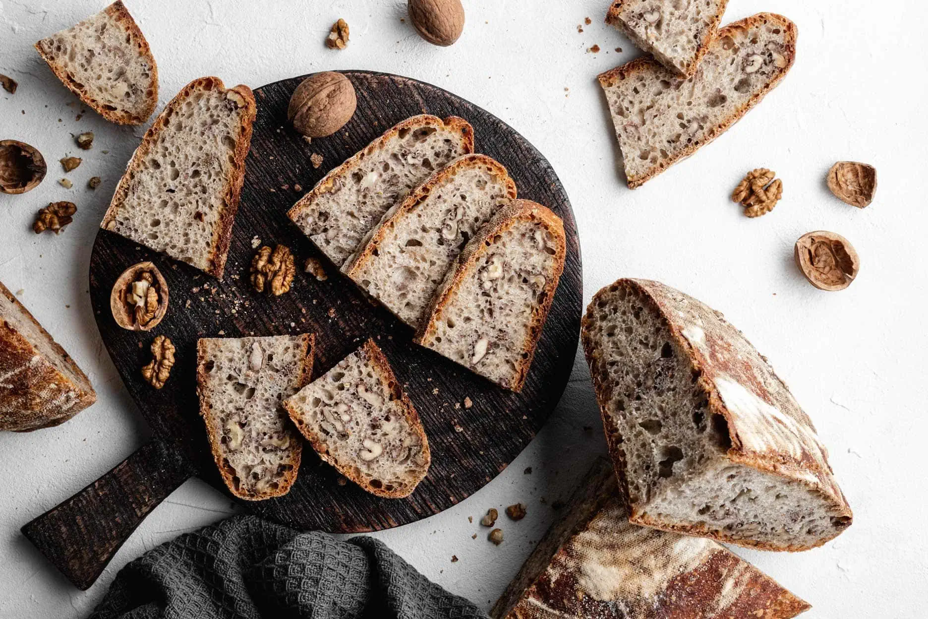 Dinkelbrot mit Walnussstücken in Scheiben geschnitten auf einem Brett. Daneben liegen Walnussschalen und Walnüsse.