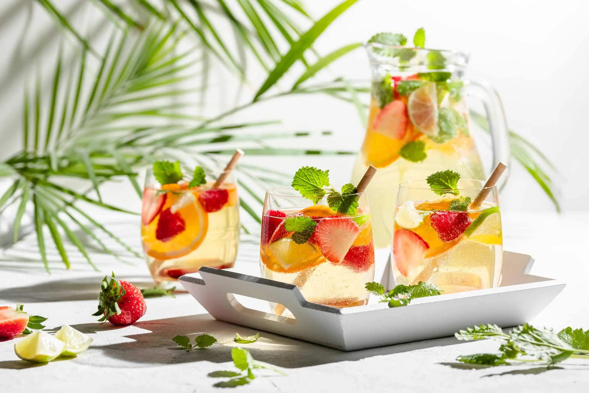 Weiße Sangria mit frischen Früchten garniert mit Zitronenmelisse in Gläsern und einer Karaffe.