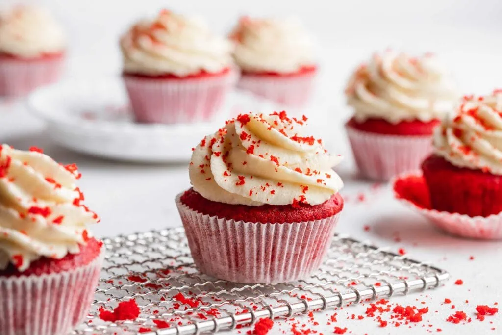 Red Velvet Cupcakes mit Frischkäse-Frosting auf einem Gitter. Auf dem Frosting sind rote Brösel.