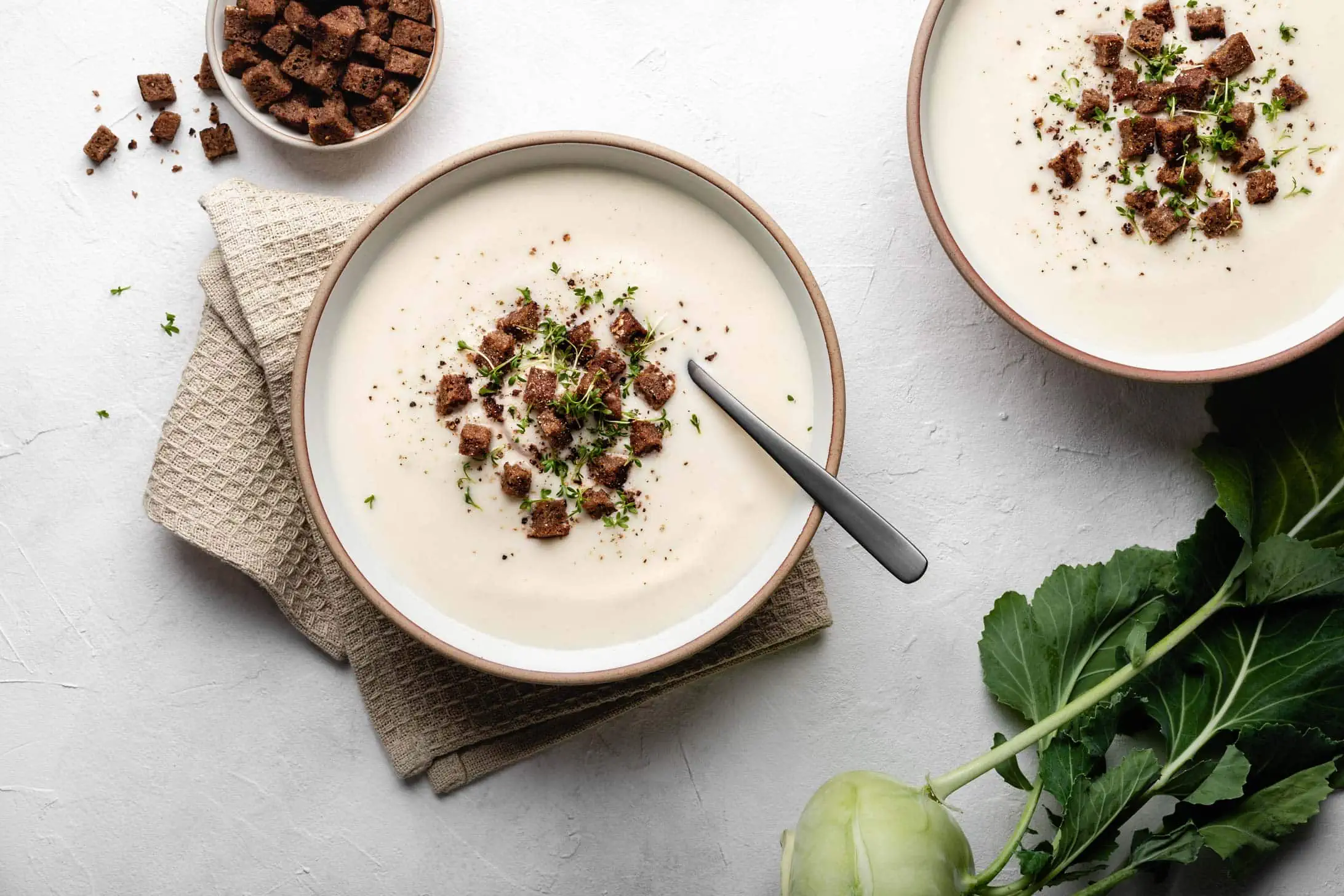 Zwei Teller gefüllt mit einer cremigen Kohlrabisuppe mit einem Topping aus Croûtons und frischer Kresse.