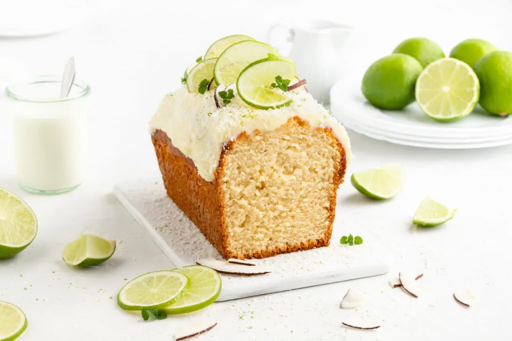 Ein saftiger Limettenkuchen mit Kokos und einem cremigen Frischkäse-Frosting liegt auf einer weißen Platte.
