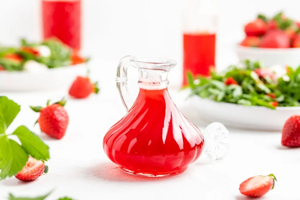 Selbstgemacher Erdbeeressig in einer kleinen Flasche. Im Hintergrund liegen frische Erdbeeren.