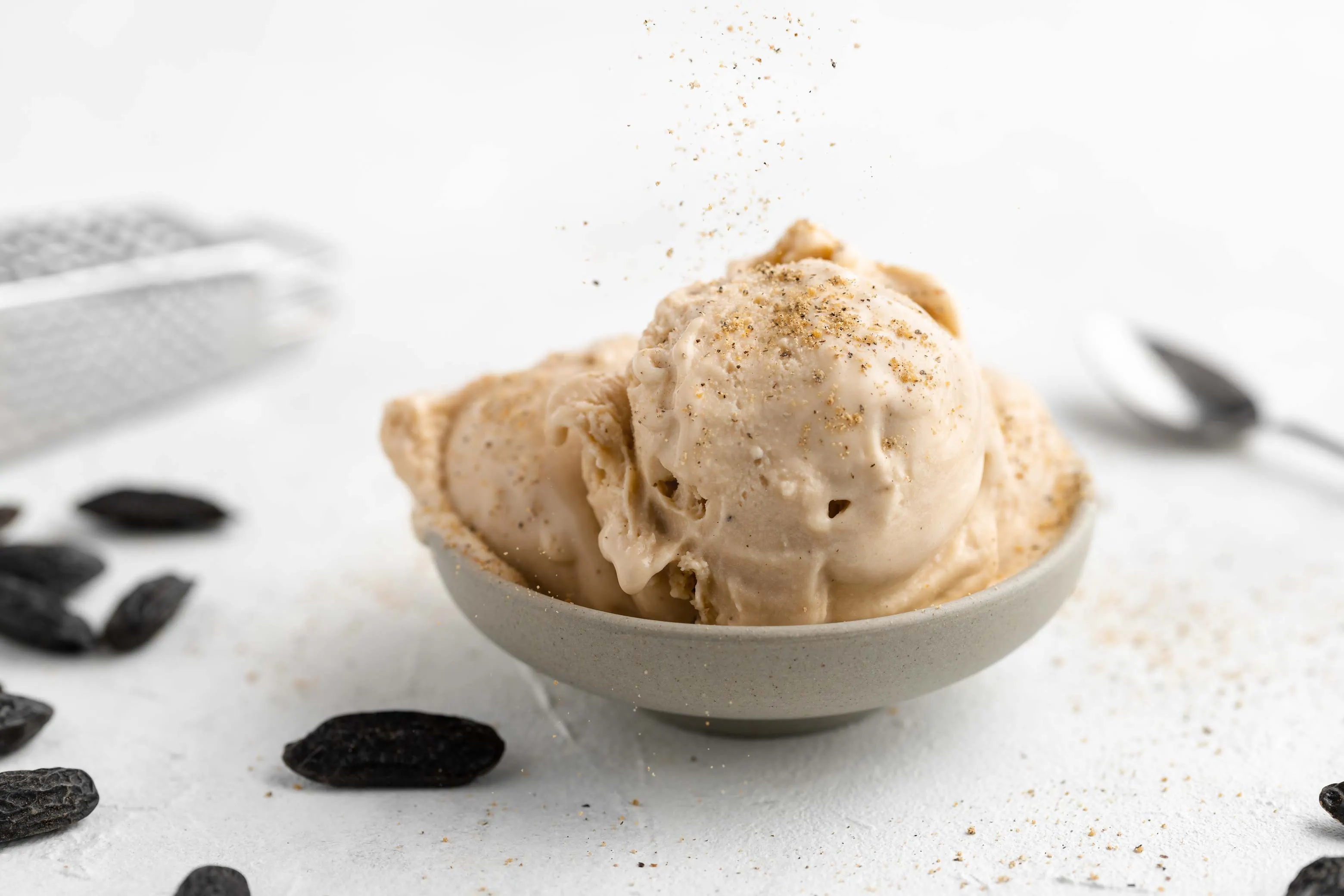 Ein Schälchen mit mehreren Kugeln cremigen Tonkabohneneis. Auf das Eis wird gemahlene Tonkabohne gestreut.