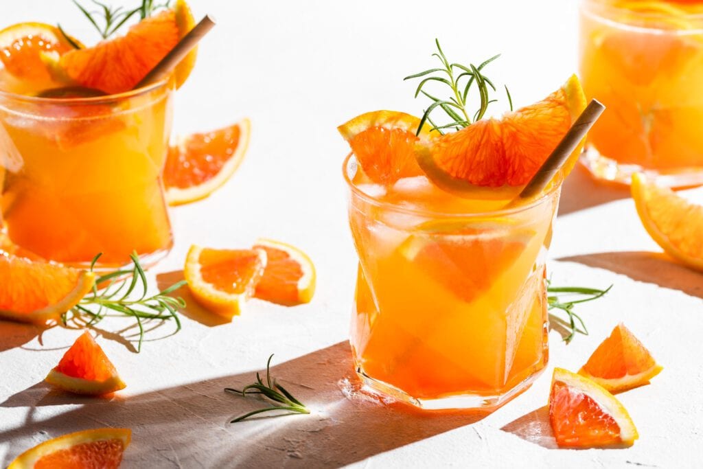 Das Trendgetränk Gin Spritz mit Aperol und Prosecco in Gläsern, garniert mit Orangenscheiben und Rosmarin.