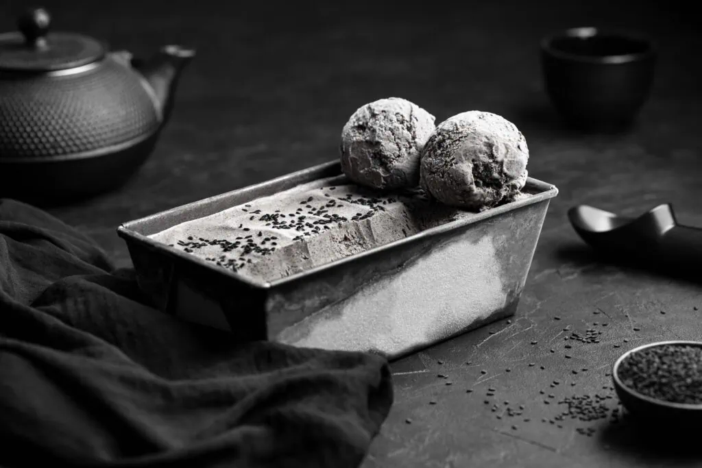 Das schwarze Sesameis aus der Eismaschine auf einem dunklen Untergrund. Neben dem Eis liegt ein Eisportionierer.