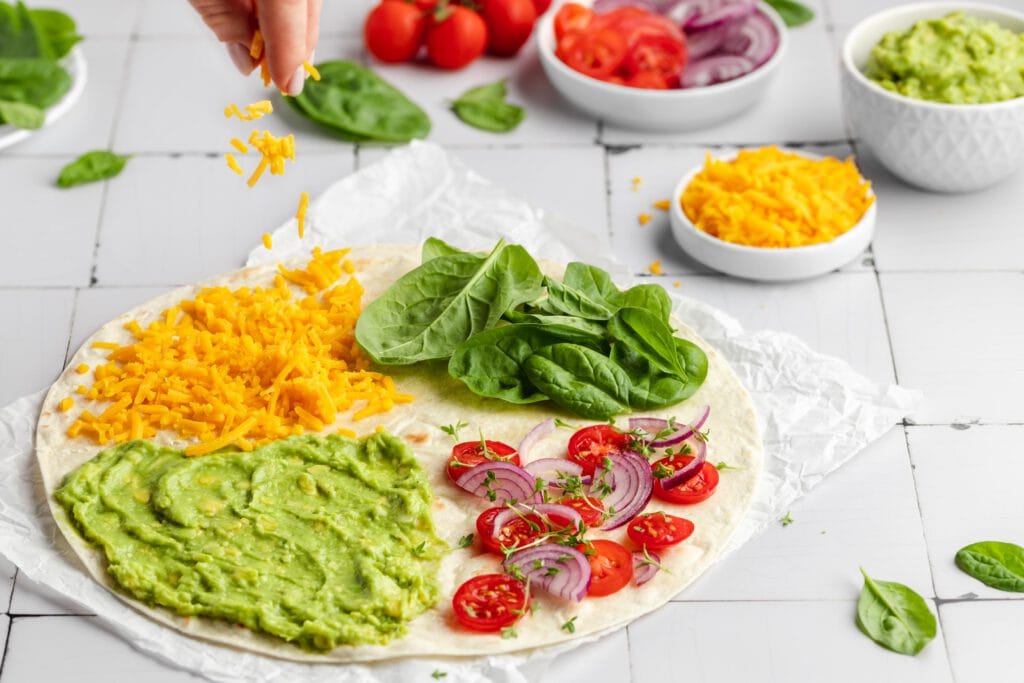 Ein Wrap mit Guacamole, Spinat, Tomaten, Zwiebeln und Käse, der nach dem TikTok-Trend gefaltet wird.