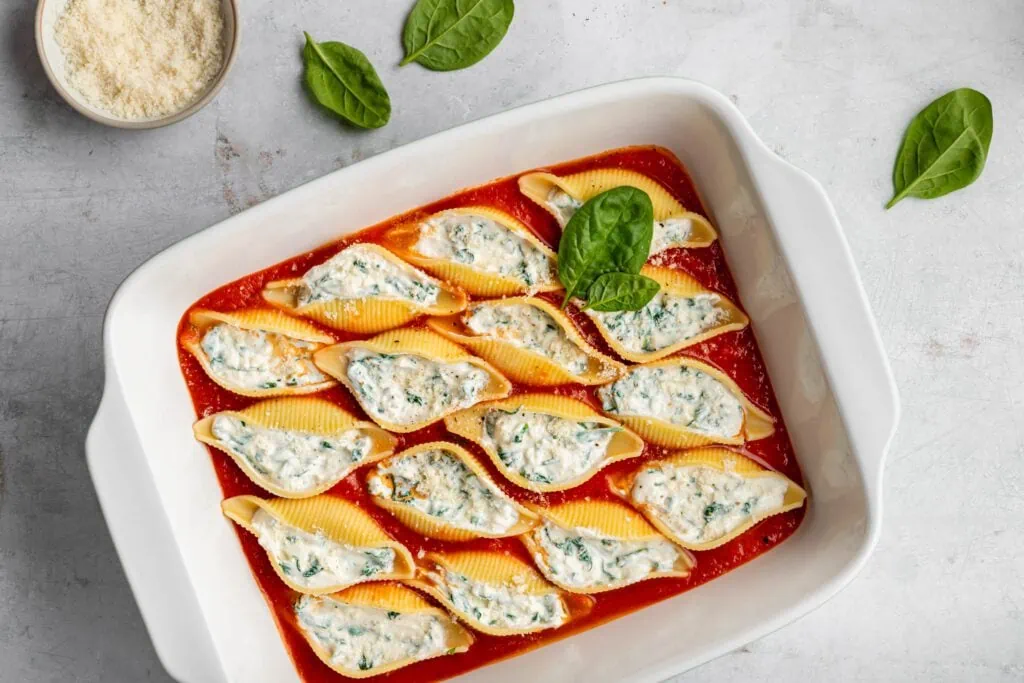 Gefüllte Muschelnudeln mit Spinat, Ricotta, Parmesan und Tomatensoße in einer Auflaufform.