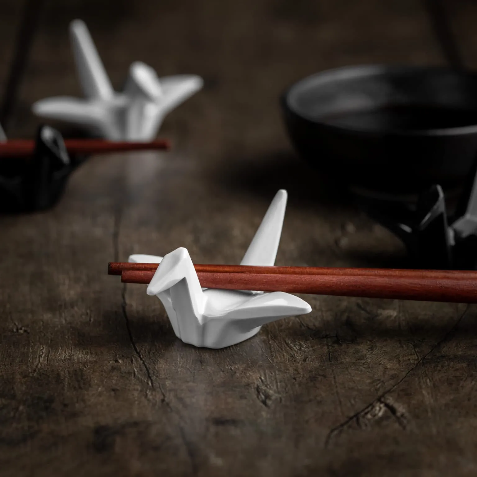 Mehrere Essstäbchen Ablagen in Form von Origami-Kranichen auf einem hölzernen Untergrund.